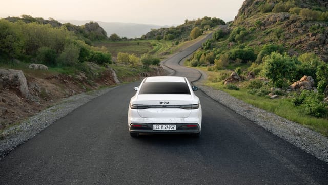 A white car travels down a winding road in the lush hills of Shaqlawa, Iraq, showcasing serene scenery.