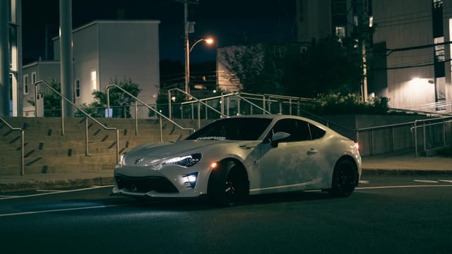A modern sports car parked under streetlights in an urban setting at night.