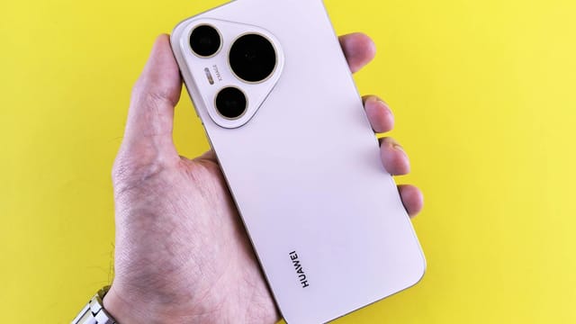 Close-up of a hand holding a modern smartphone with a yellow backdrop.