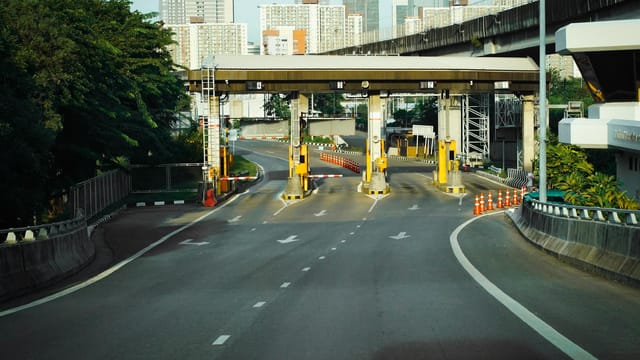 Toll booth on a Bangkok highway with urban skyscrapers in the background, during a clear day.