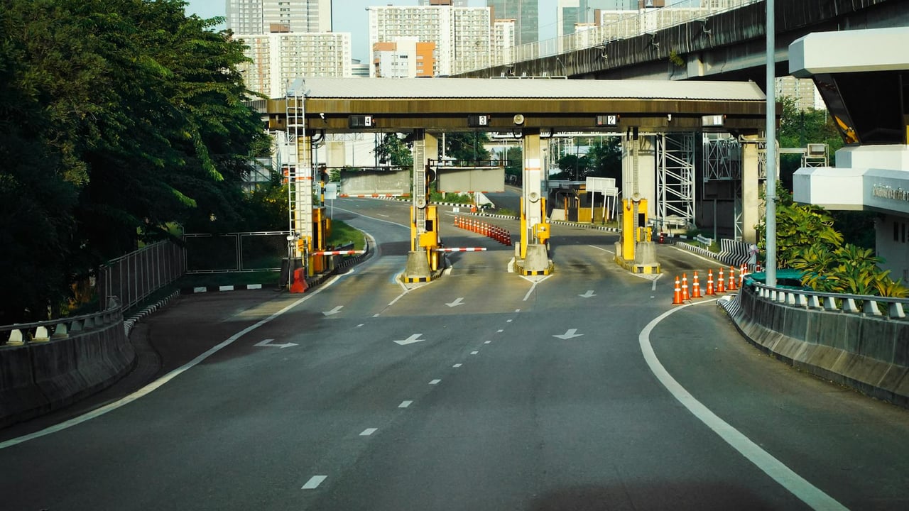 Toll booth on a Bangkok highway with urban skyscrapers in the background, during a clear day.