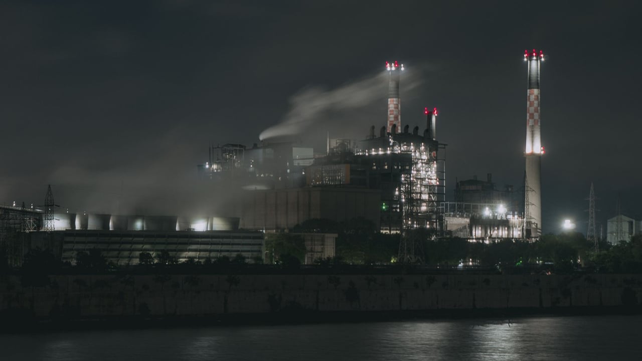 Night view of a large industrial factory with chimneys emitting smoke by the river in Ahmedabad, India.