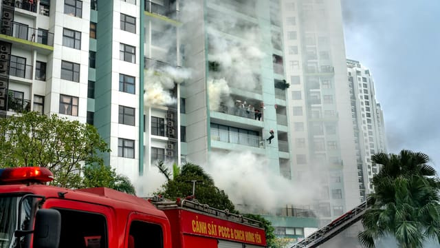 Firefighters respond to a building fire with smoke and emergency vehicles in an urban area.