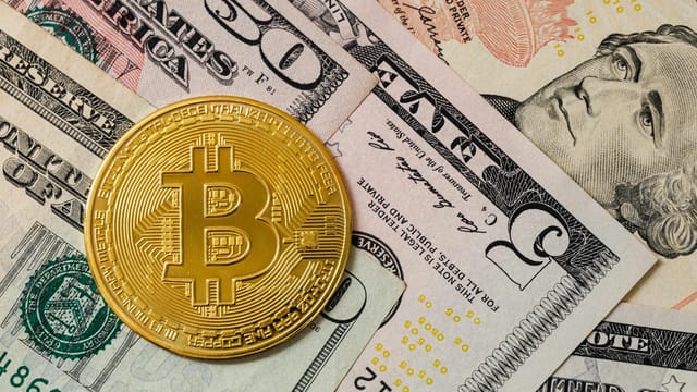 Close-up of a gold Bitcoin coin placed on various US dollar bills, illustrating digital currency concepts.