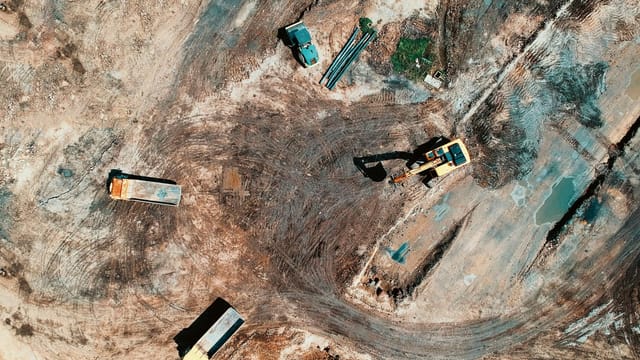 High-angle aerial view of construction site with earthmoving equipment and trucks.