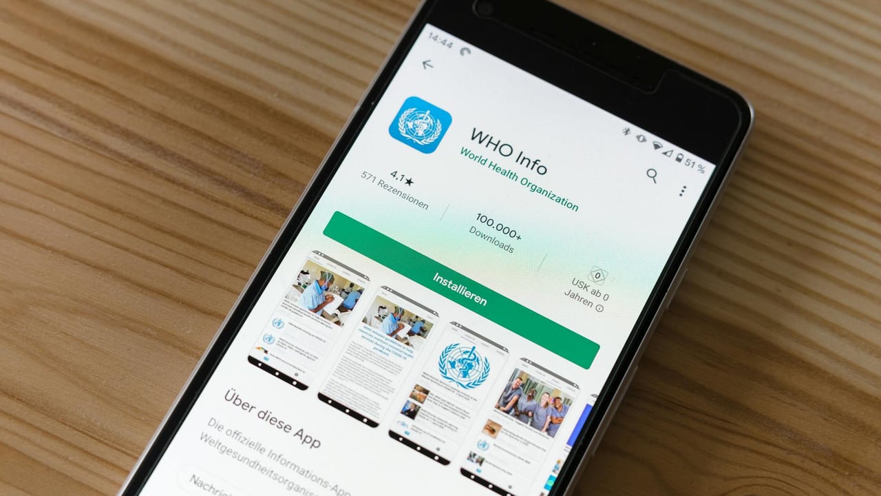 Mobile phone on wooden table showing installation screen for WHO Info app from World Health Organization.