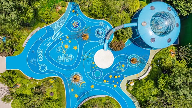 Aerial shot of a vibrant, space-themed playground with blue designs and surrounding greenery.