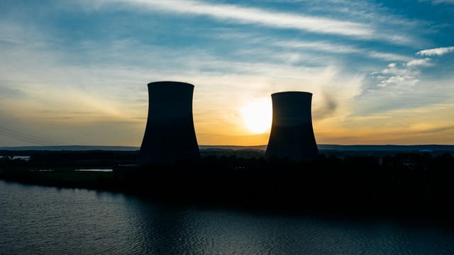 Identical cooling tower silhouettes on power plant near rippled river under colorful cloudy sky at sundown