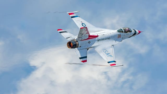 US Air Force jet performing aerobatic maneuvers against a clear blue sky, showcasing speed and agility.