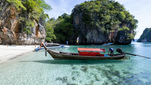 Peaceful Thai beach with clear waters, longtail boat, and limestone cliffs. A perfect tropical escape.