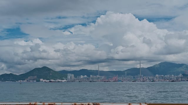 Dramatic cityscape with ocean and mountains under cloudy sky.