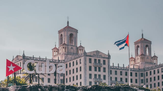 View of the historic Hotel Nacional in Havana, Cuba with a waving Cuban flag and clear sky.