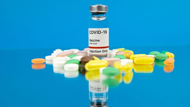 Conceptual image of COVID-19 vaccine with pills symbolizing hope for cure on reflective surface.