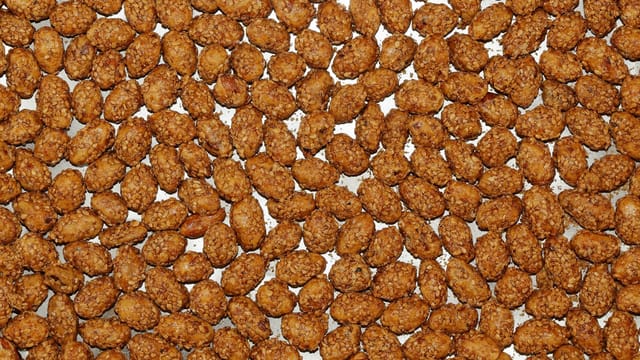 A detailed view of roasted candied almonds on a baking sheet, showcasing their crunchy texture.