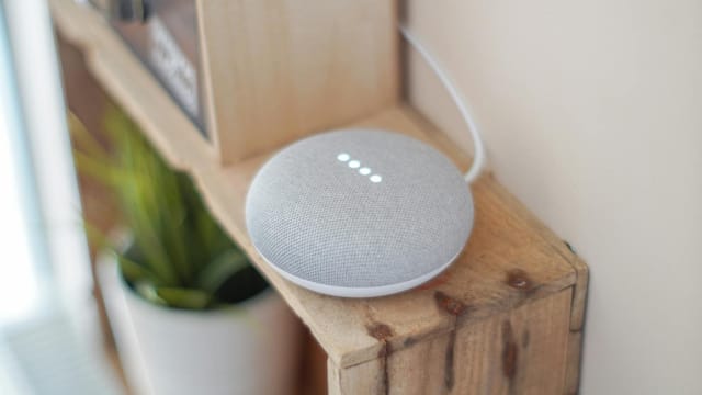 A Google Home Mini smart speaker on a wooden shelf, blending technology with home decor.