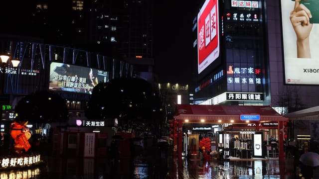A bustling city center at night with bright billboards and wet pavements reflecting vibrant lights.