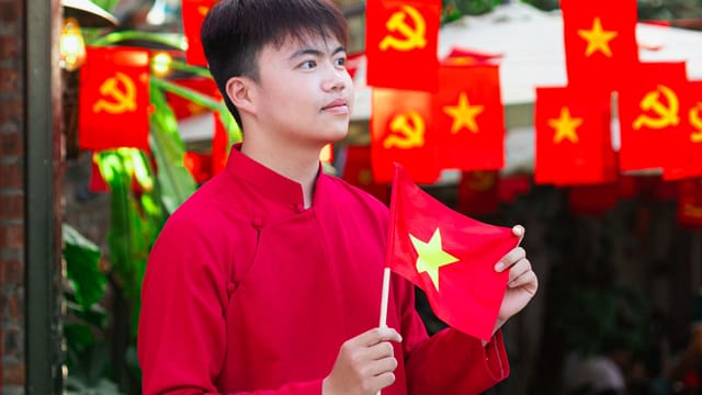 Young man in traditional attire holding Vietnam flag, celebrating National Day with vibrant decorations.