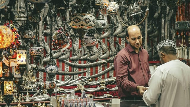 A bustling Omani market stall filled with traditional lamps and daggers, showcasing vibrant culture.