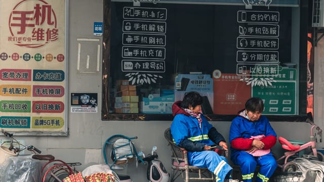 Two workers in blue uniforms rest outside a mobile repair shop with signage.