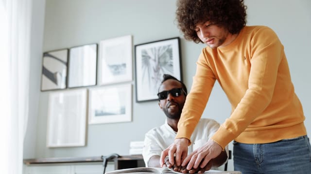 Two men engaged in Braille reading, promoting assistive technology and independence.
