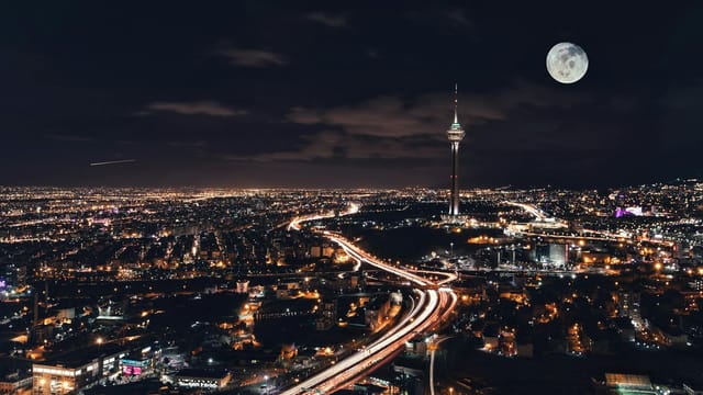 Captivating night view of Tehran's skyline featuring Milad Tower and a full moon.