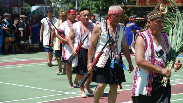A group of men in traditional attire perform an outdoor cultural dance, showcasing vibrant costumes and ceremonial elements.