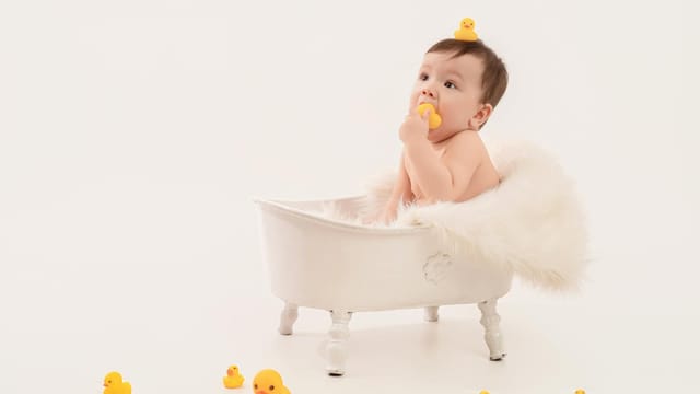 Cute baby sitting in a bathtub surrounded by rubber ducks, creating a playful and joyful scene.