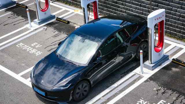 A black Tesla parked at a charging station in an urban setting.