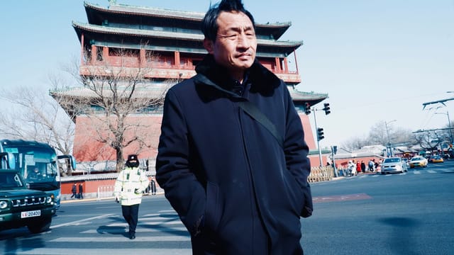 Man walking near Beijing's historic Bell Tower on a sunny day.