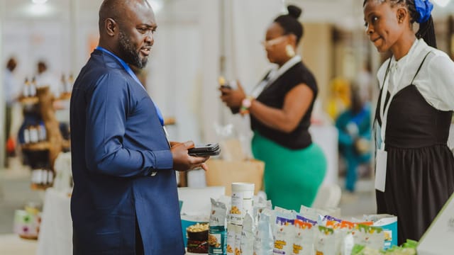 Business professionals interacting at a trade show in Accra, Ghana, showcasing products and engaging in conversation.