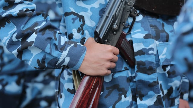 Close-up of hand holding a rifle in blue camouflage uniform, outdoors.