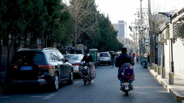 A bustling Beijing street with cars, scooters, and people, capturing urban life in daylight.