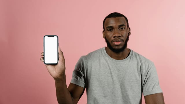 Man in gray shirt holding a smartphone with a blank screen, set against a pink background.