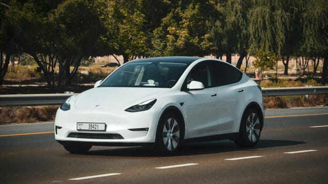 A sleek white electric car cruising on a sunny highway in Abu Dhabi, UAE.