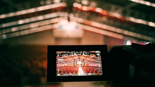 A digital camera screen captures an empty auditorium with rows of red seats under warm lighting.