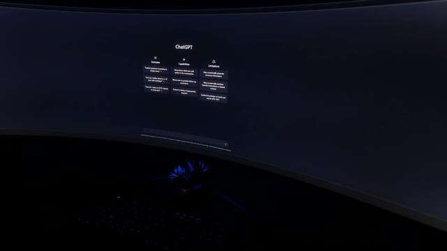 Close-up of a dark room with a curved monitor showing the ChatGPT interface on screen.