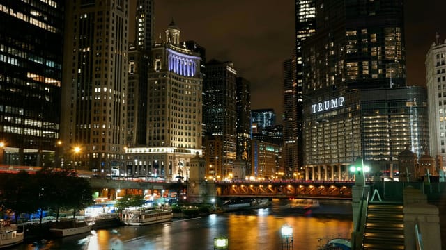 Illuminated Chicago skyscrapers and river at night with iconic bridge view.