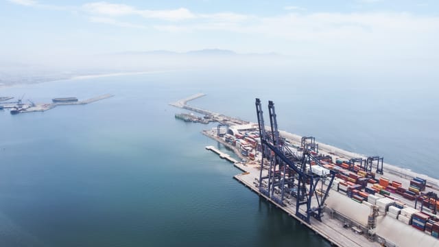 A sweeping aerial shot capturing logistics and container ships at Ensenada Port, Baja California.