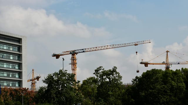 Cityscape featuring multiple tower cranes and a modern building under a clear blue sky.