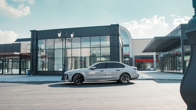 A sleek silver car parked in front of a modern shopping mall on a sunny day.