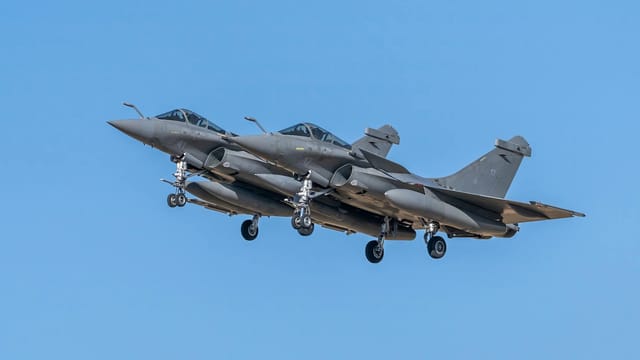 Two Rafale fighter jets in flight over Los Llanos, Spain, against a bright blue sky.
