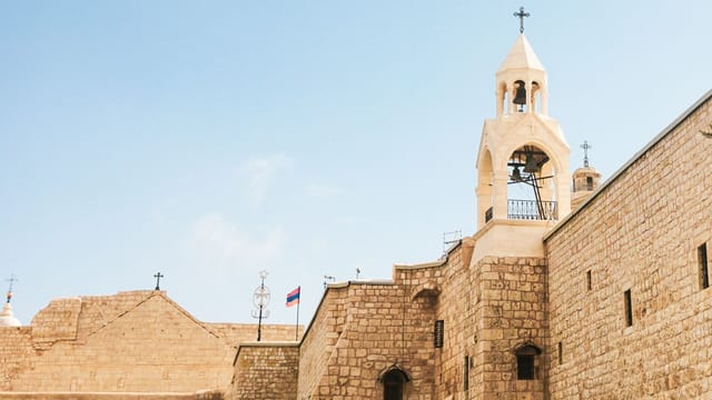 Stone facade of a historical church in Bethlehem under a clear blue sky.