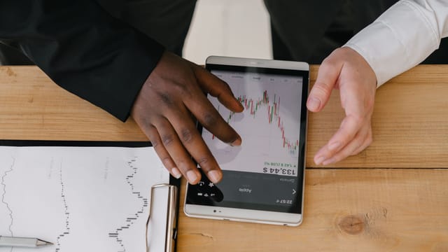 Two professionals analyzing stock market trends on a tablet in an office setting.