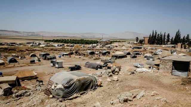 Aerial view of a refugee camp in Idlib, Syria with tents and arid terrain under a clear sky.