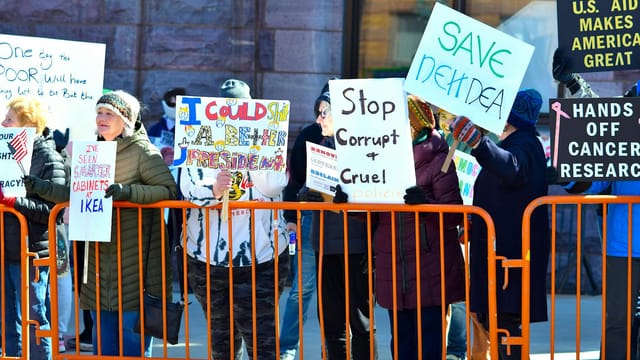 A group of people holding signs in a street protest, expressing dissent against political policies.