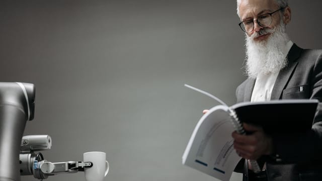 Elderly man reads as a robotic arm holds a coffee cup, showcasing technology integration.