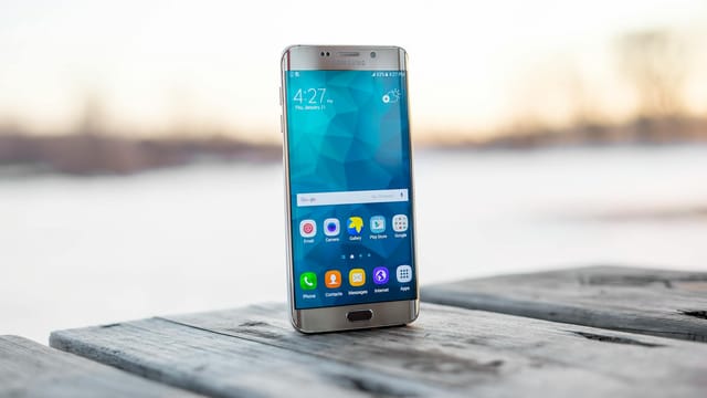 Samsung smartphone placed on a wooden surface outdoors during sunset.