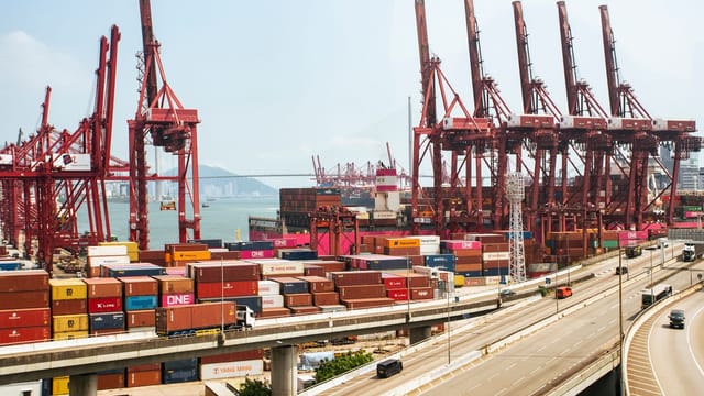 A vibrant view of Hong Kong's bustling shipping port with red cranes and stacked containers.
