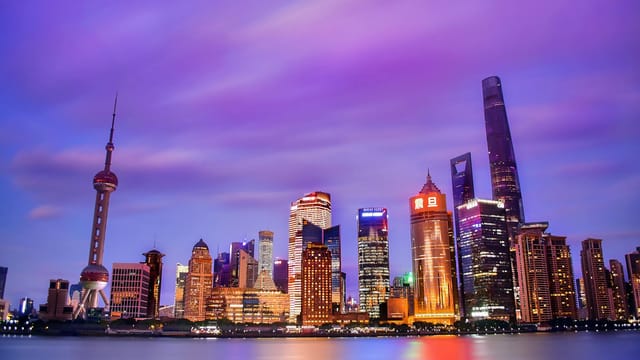 A vibrant skyline of Shanghai's modern skyscrapers reflected in the water during dusk.