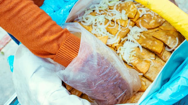 Person retrieving crispy snacks from a plastic bag at an outdoor market.